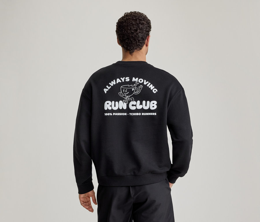 Muž zozadu v čiernej mikine s bielym nápisom 'ALWAYS MOVING RUN CLUB' a kreslenou bežiacou šálkou kávy na chrbte.