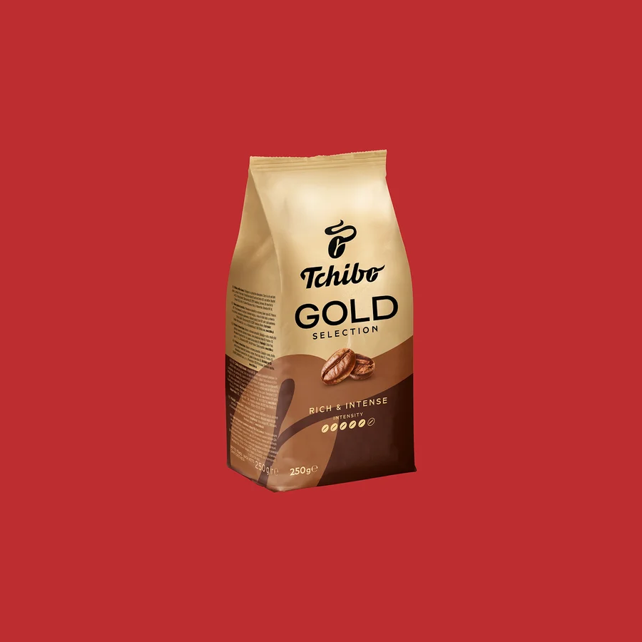 Béžovo-hnedé balenie kávy Tchibo Gold Selection s nápisom „RICH & INTENSE“, kávovými zrnami a hmotnosťou 250g, na červenom pozadí.