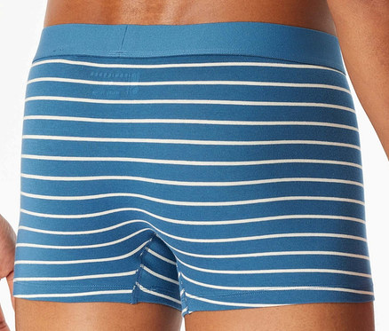 Muž pózuje v modrých boxerkách s bielymi prúžkami.