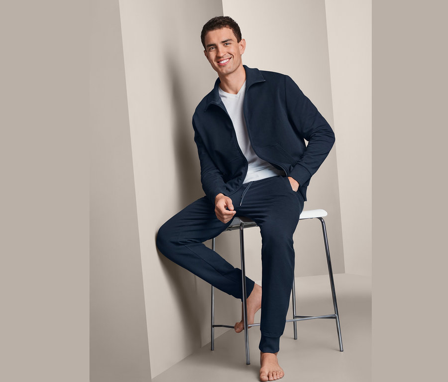 Muž sedí na stoličke a má na sebe tmavomodrú domácu súpravu.