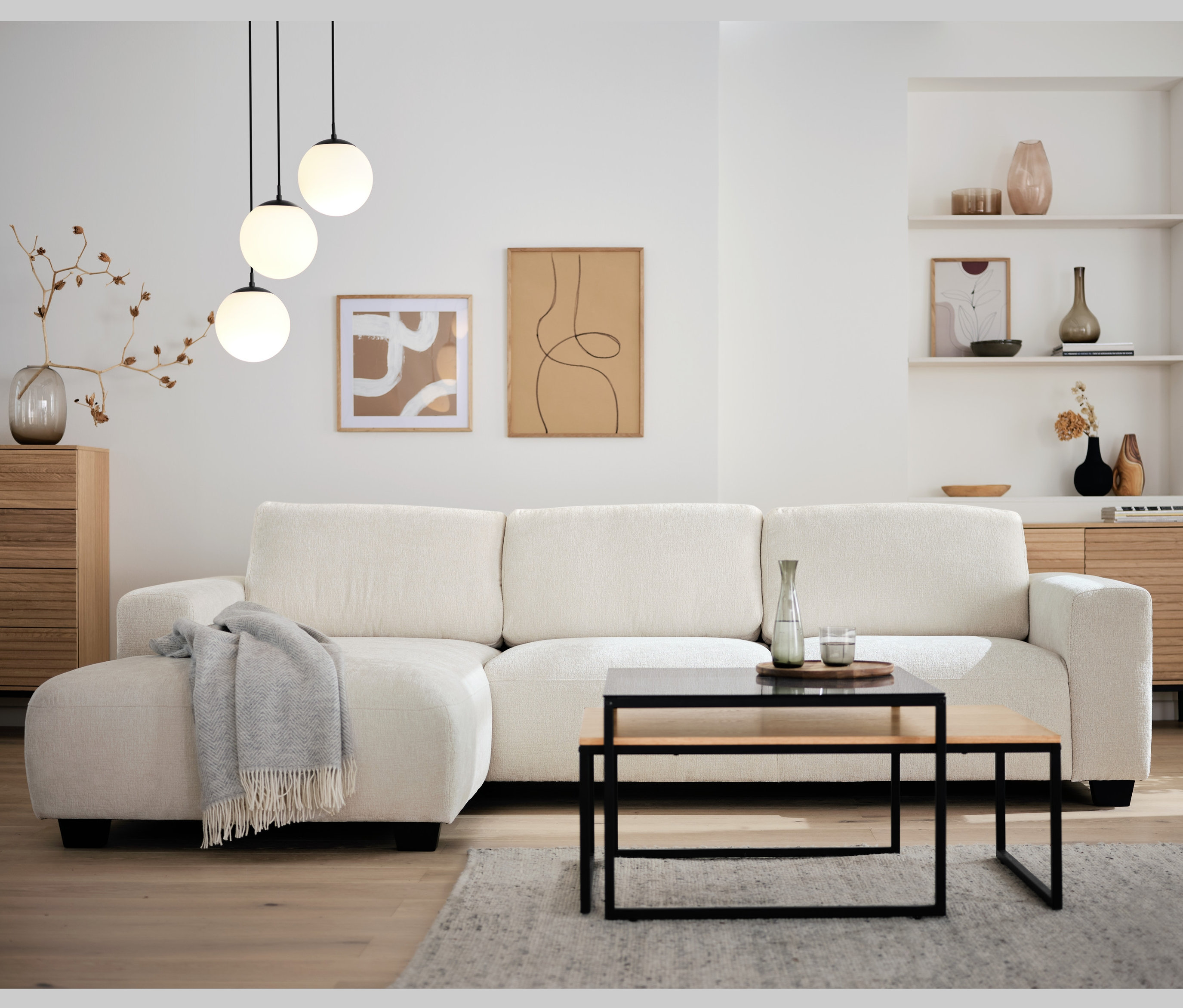 Obývacia izba s krémovou rohovou sedačkou, dvojdielnou súpravou konferenčných stolíkov a závesným svietidlom so sklenenými guľami.