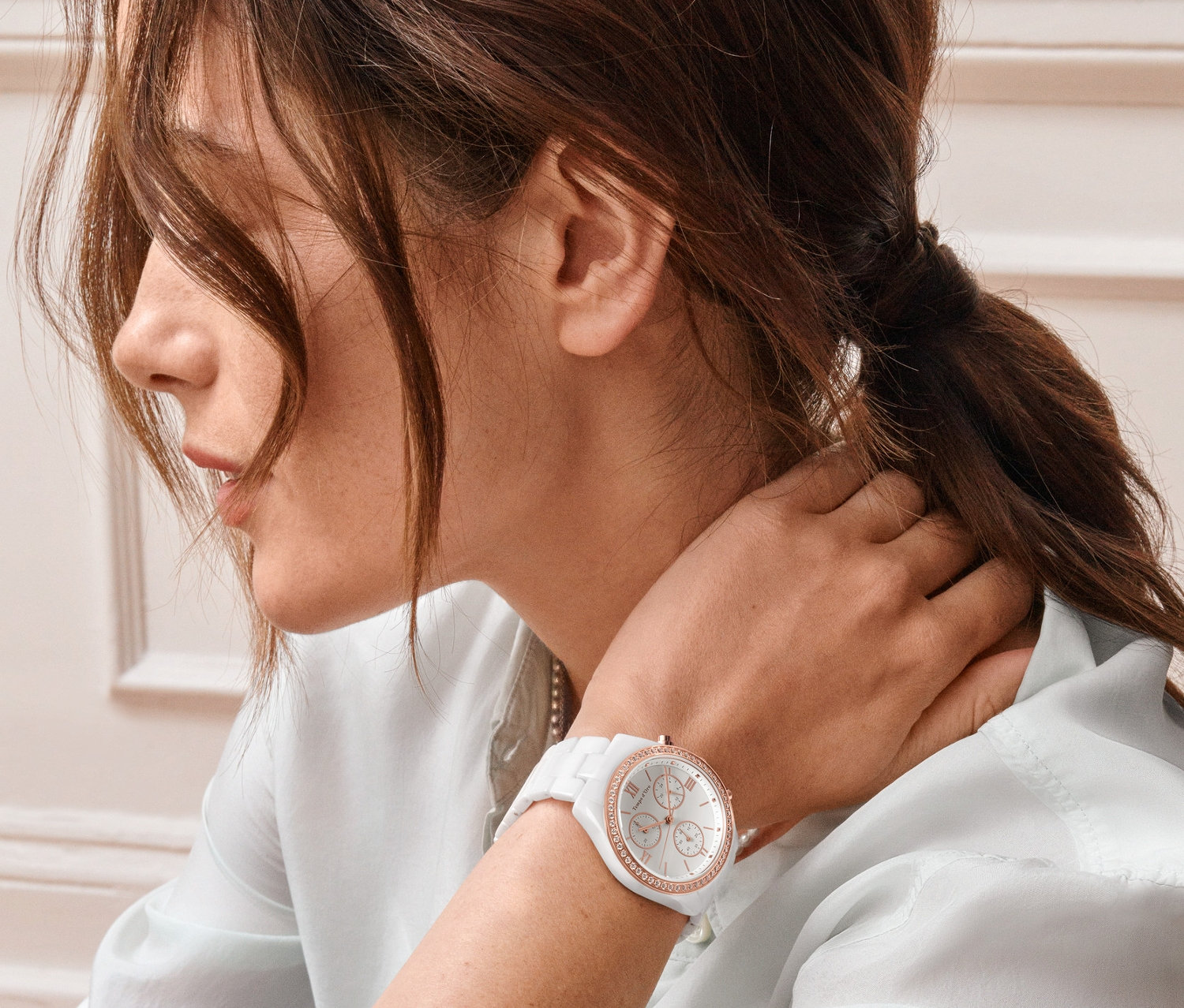 Žena sa dotýka krku a na zápästí má keramické hodinky s chronografom a zirkónmi.