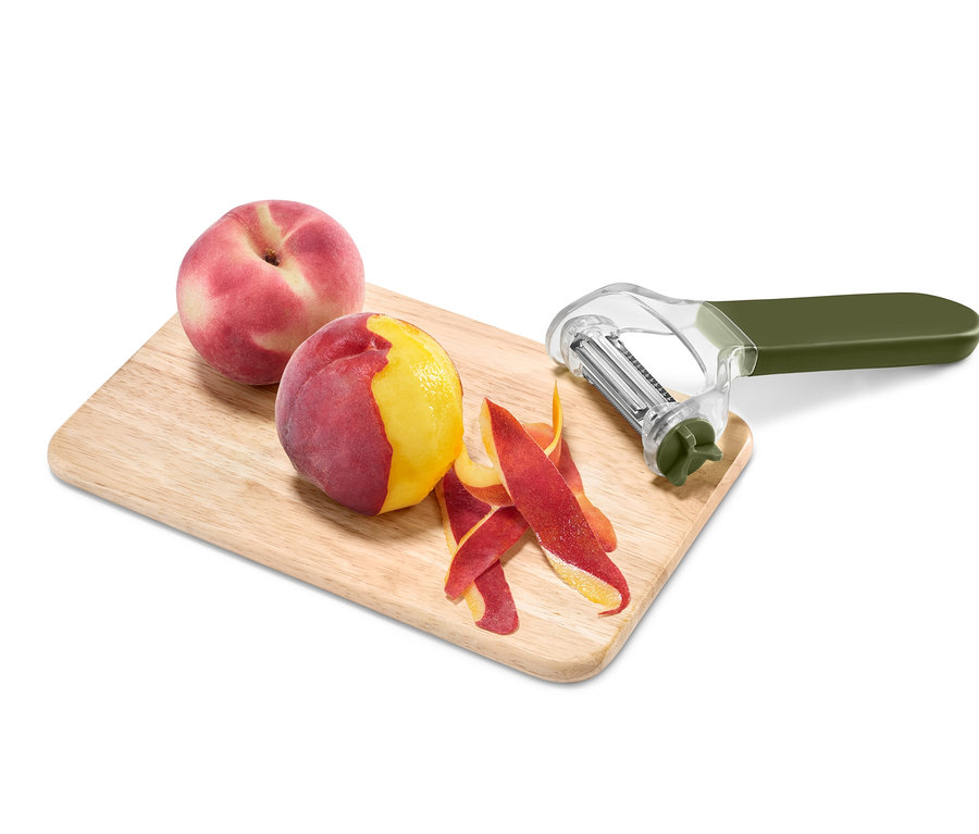 Na drevenej doske ležia broskyne a univerzálna škrabka 3 v 1.