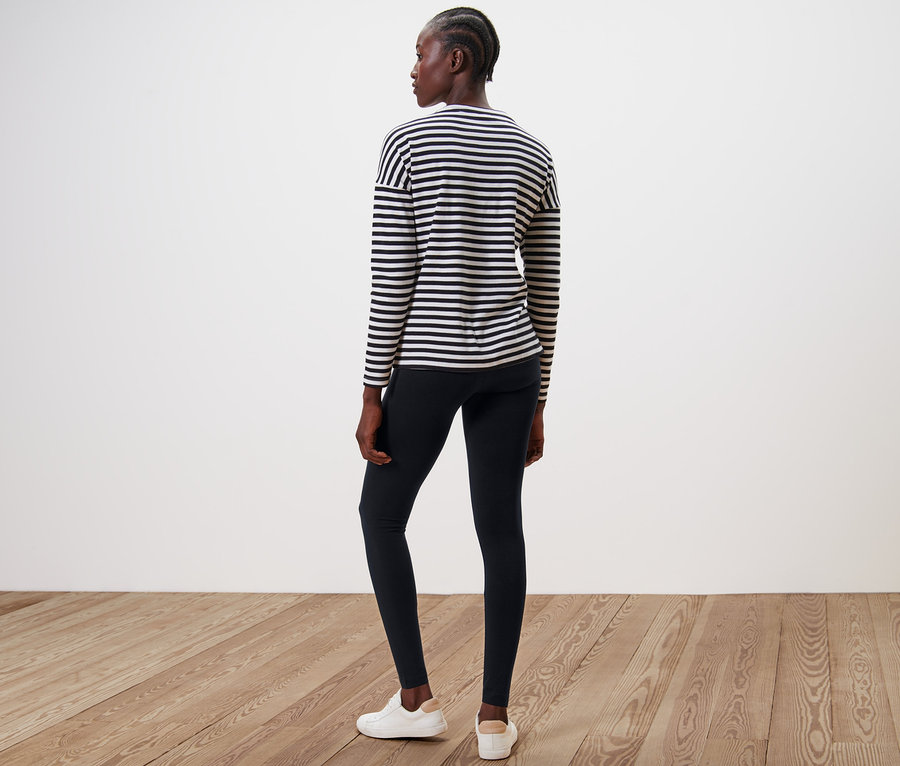 Žena stojí chrbtom k fotoaparátu a má na sebe čierne legíny a pruhované tričko.