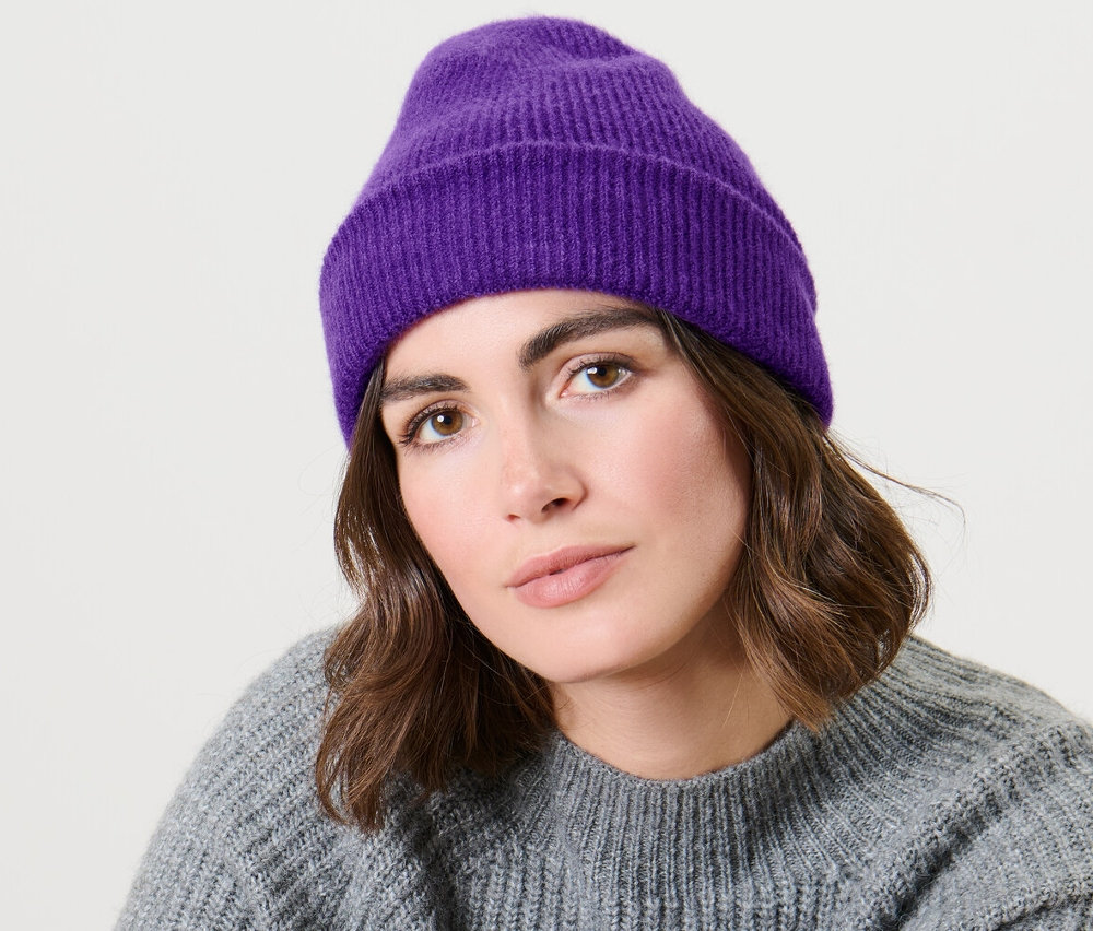 Žena sedí a má na sebe fialovú pletenú čiapku.