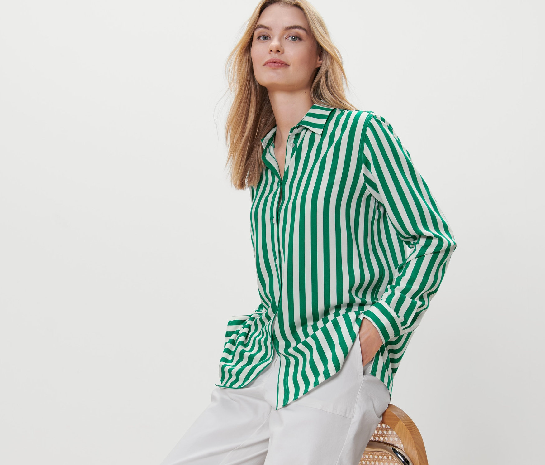 Blondínka sedí na stoličke a má na sebe zelenú prúžkovanú blúzku.