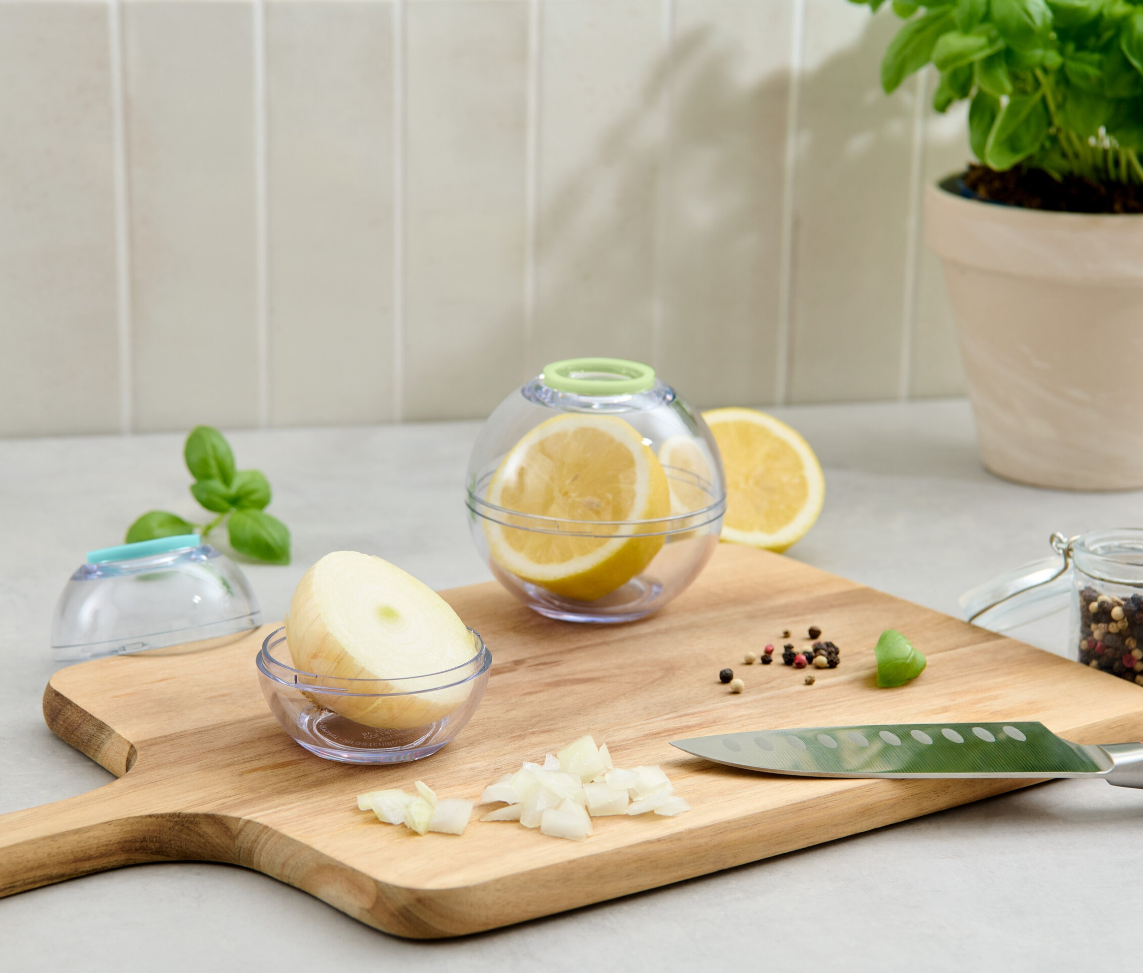 Dve guľaté nádobky na uchovávanie potravín, jedna s citrónom a druhá s cibuľou, ležia na doske na krájanie.