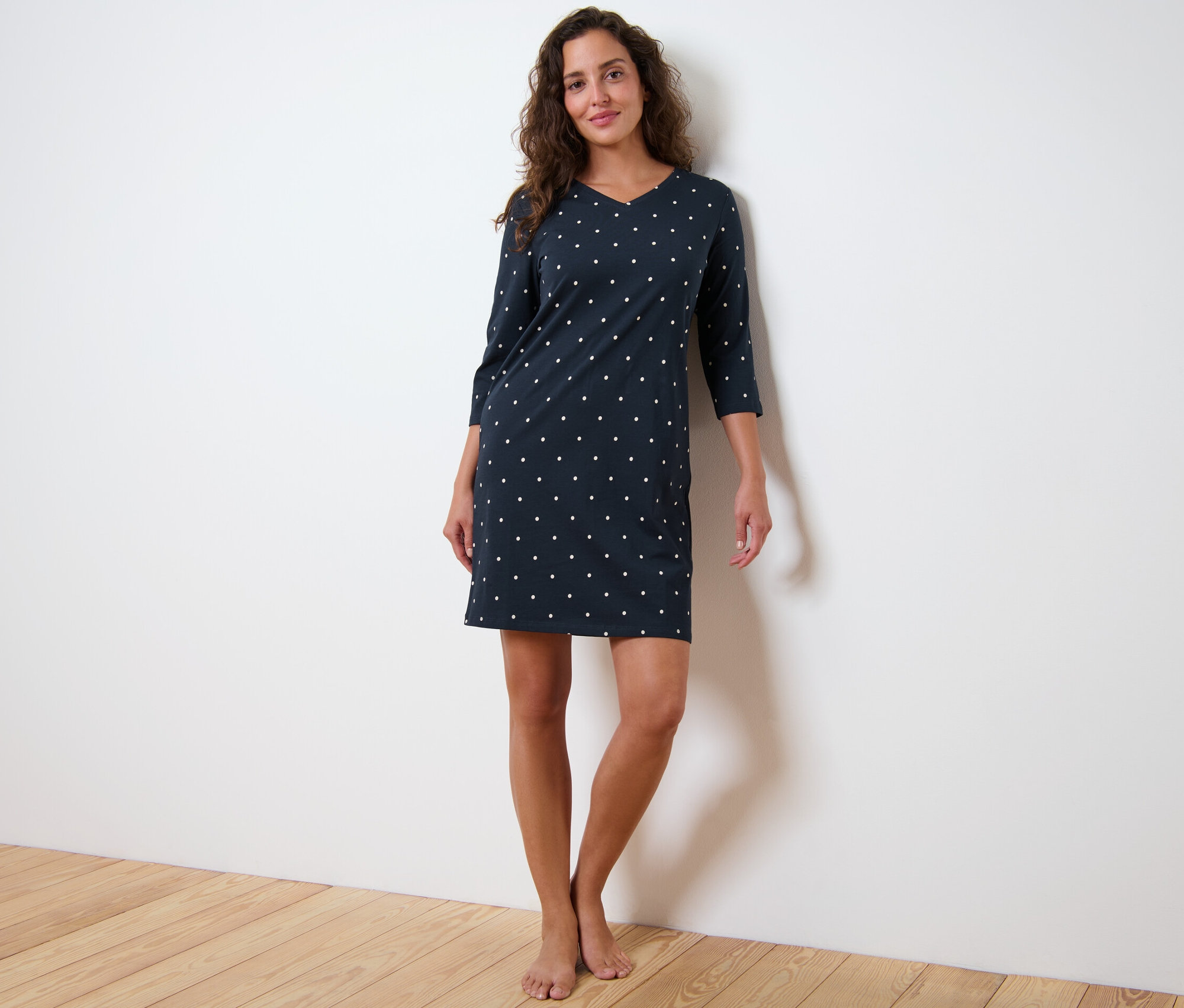 Žena stojí a má na sebe nočnú košeľu s trojštvrťovými rukávmi a bodkami.