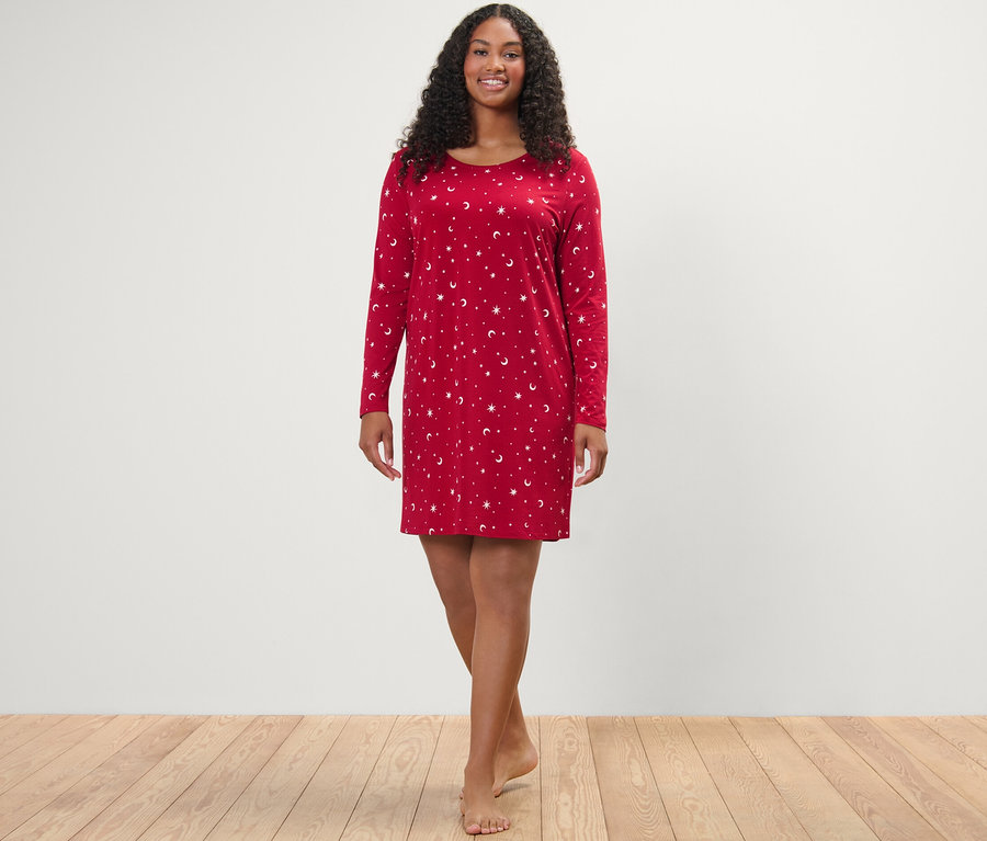 Žena stojí a usmieva sa do kamery, oblečená v červenej nočnej košeli.