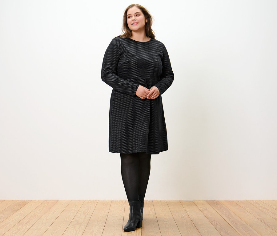 Žena stojí a má na sebe trblietavé žakárové šaty.