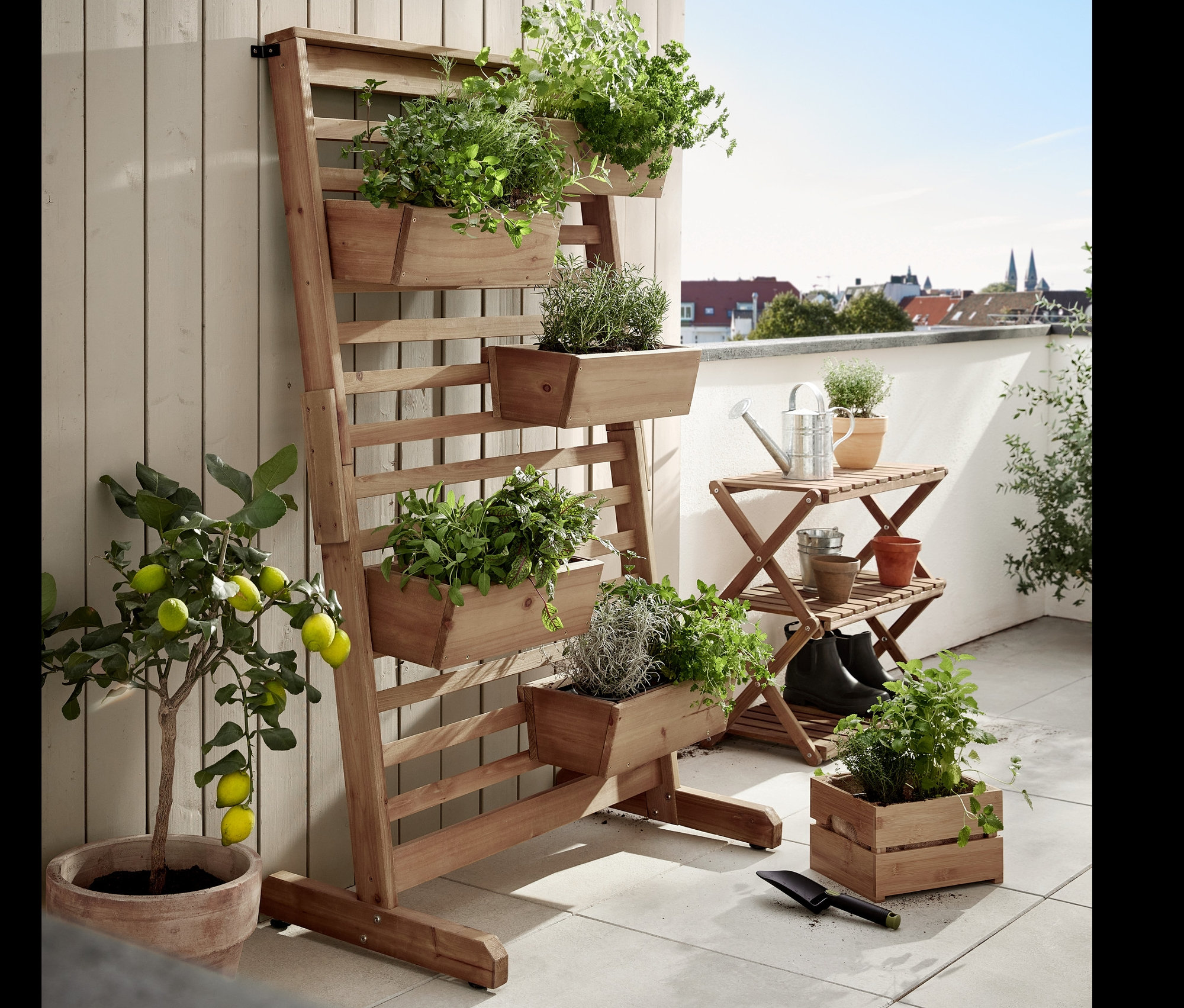 Na terase stojí skladací regál »Tinus« a vertikálny záhon »Tinus« s kvetináčmi, oba osadené zelenými rastlinami.