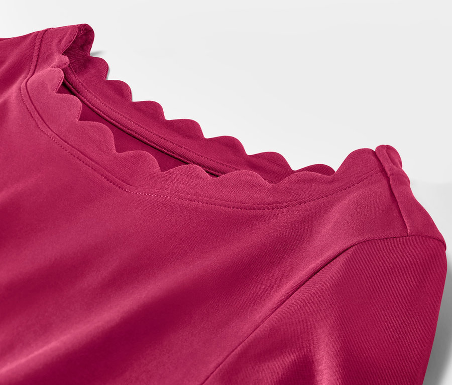 Detail malinového červeného trička s trojštvrťovým rukávom a ozdobným výstrihom.