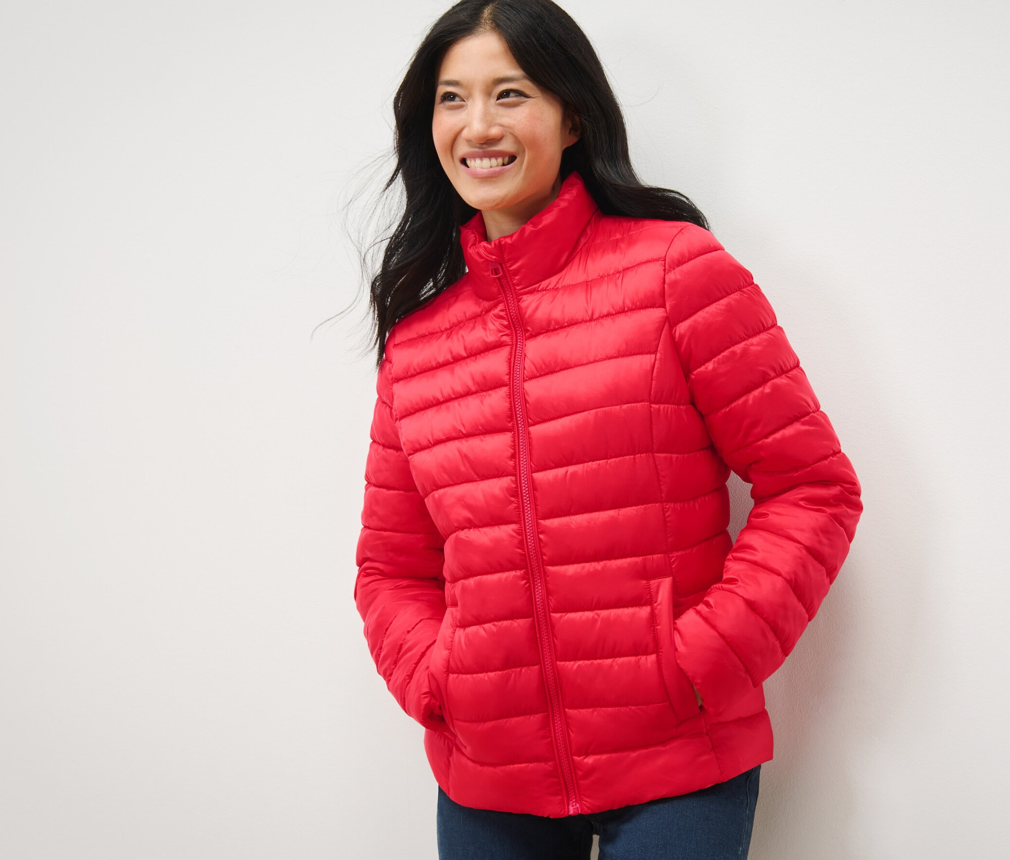 Žena sa usmieva a pózuje v červenej prešívanej bundě.