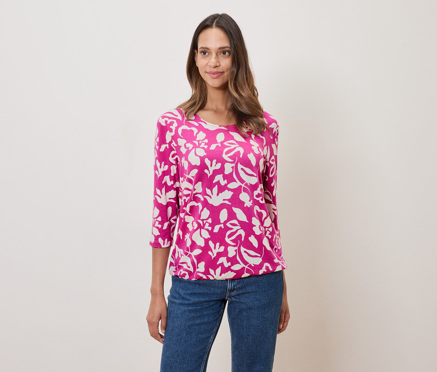 Žena má na sebe ružovú blúzku s kvetinovou potlačou a džínsy.