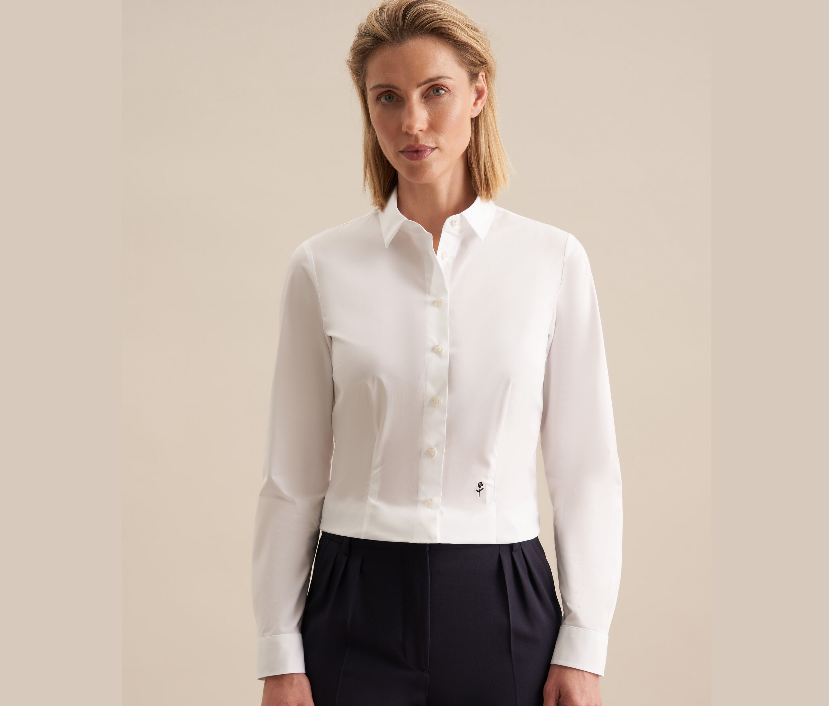 Žena má na sebe bielu slimfit blúzku Seidensticker a tmavomodré nohavice.