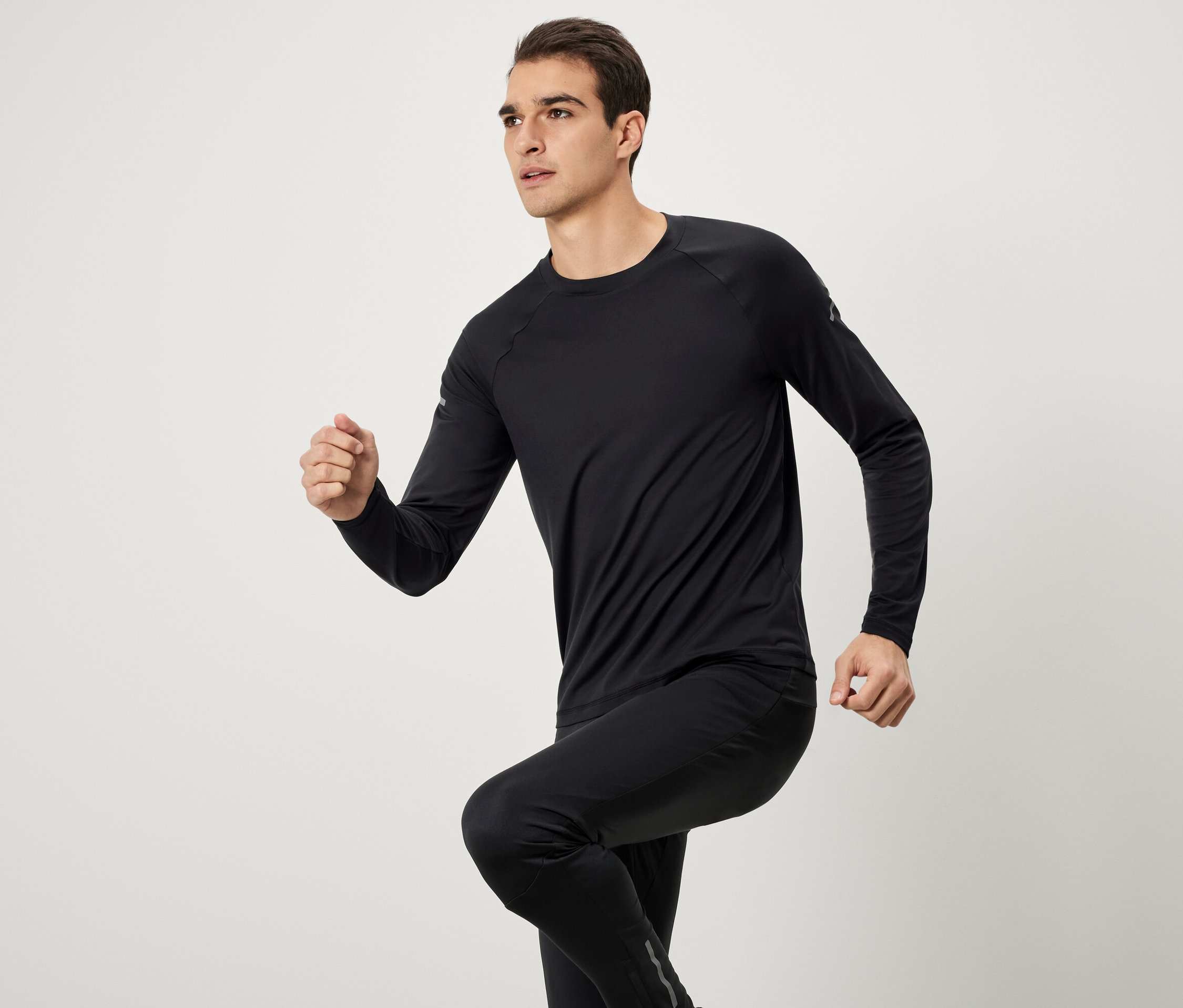 Muž v čiernom športovom oblečení s dlhým rukávom a nohavicami pri behu.