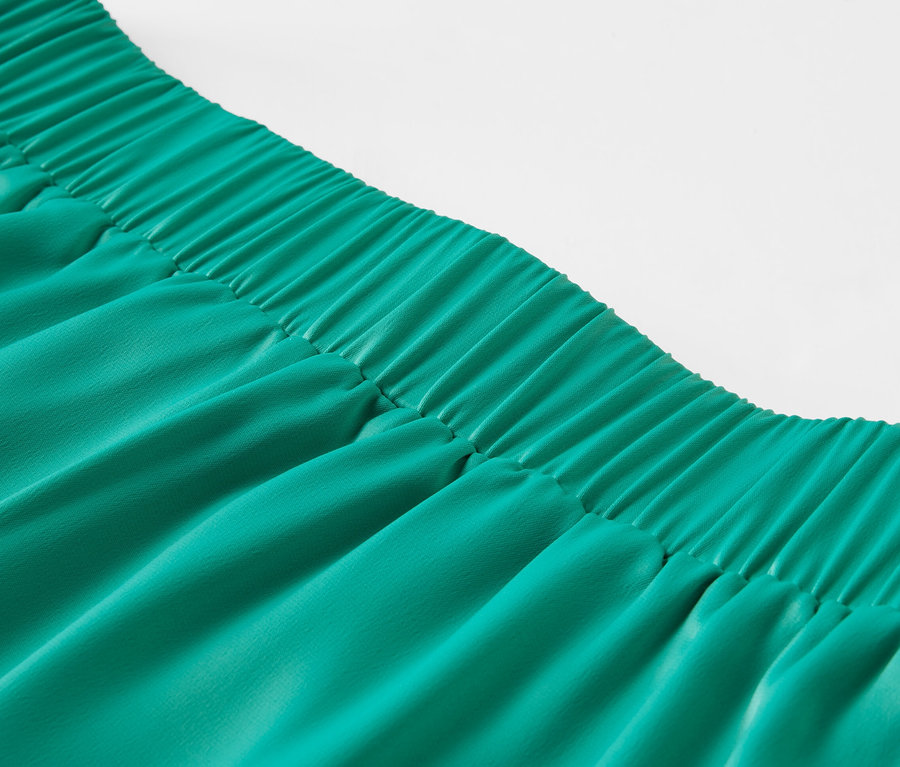 Detailný záber na zelenú saténovú sukňu s elastickým pásom.
