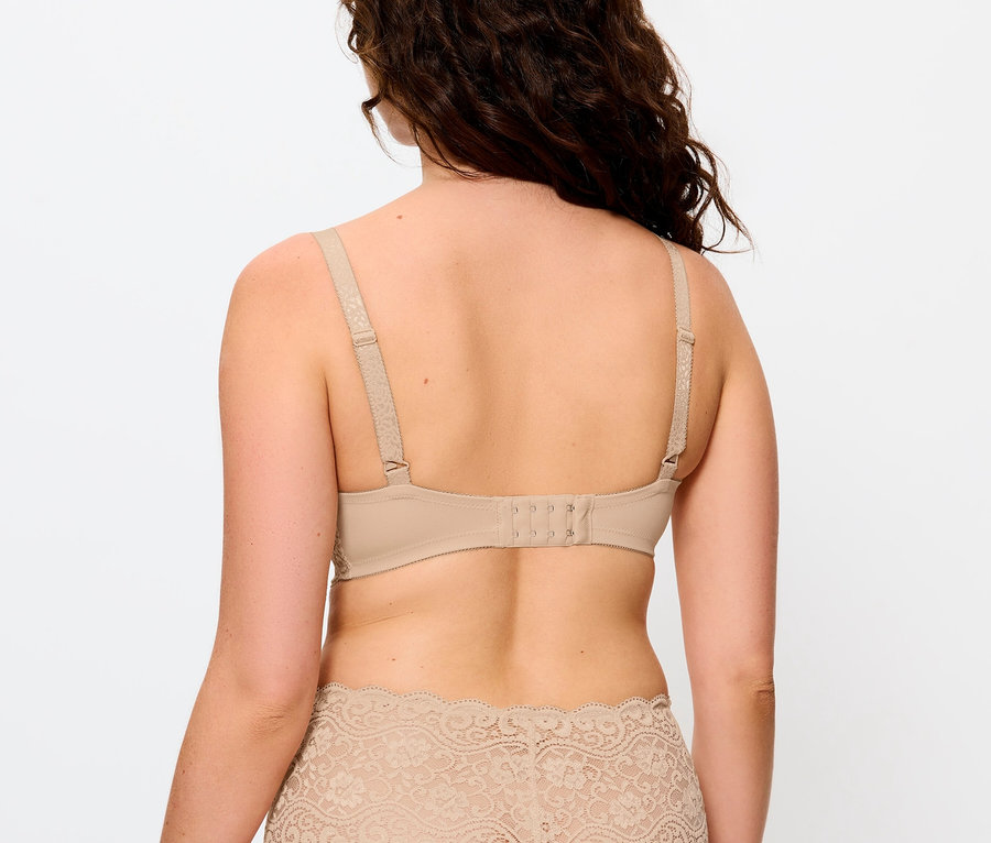 Pohľad zozadu na ženu s hnedými vlnitými vlasmi, ktorá má na sebe béžovú podprsenku a nohavičky s čipkou.