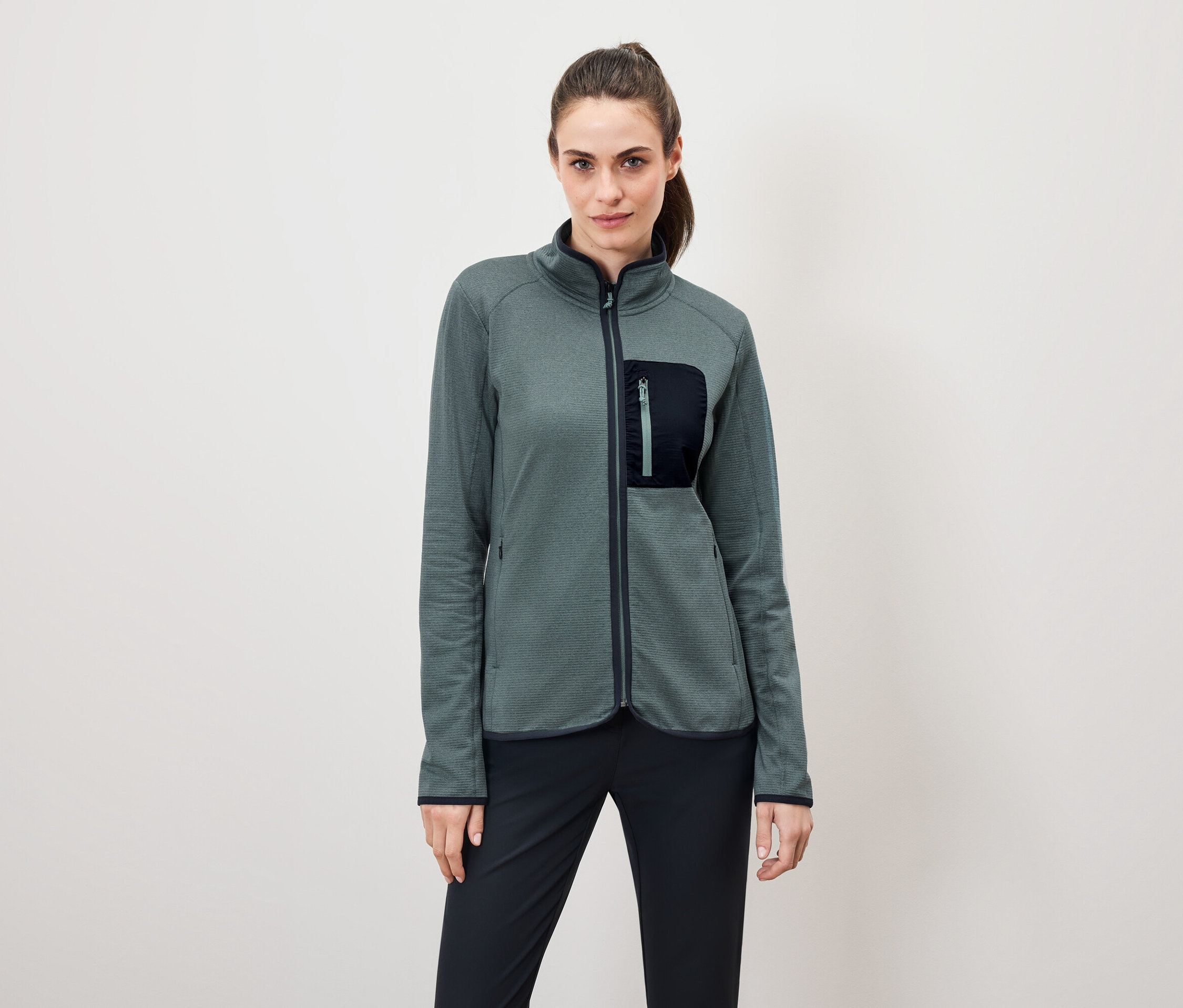 Žena má na sebe zelenú fleecovú bundu a čierne nohavice.