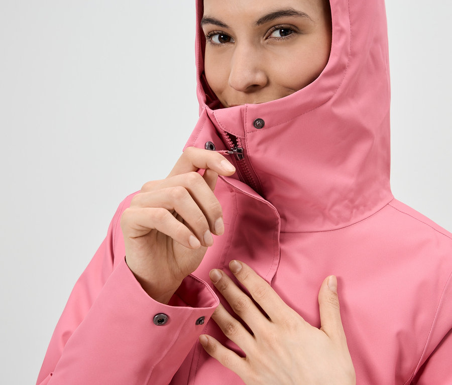 Žena si zapína zips na ružovej pršiplášti s kapucňou.