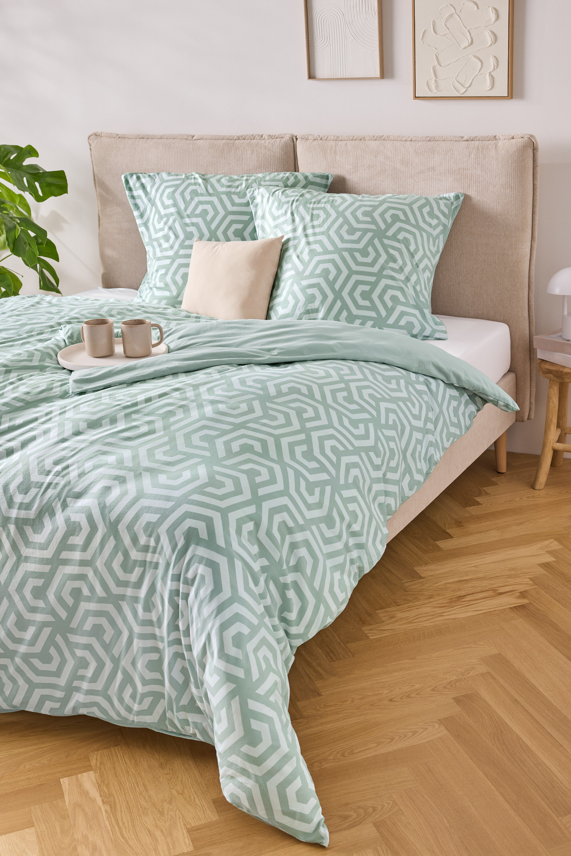 Posteľ s bledomodro-bielou pruhovanou posteľnou bielizňou, dvoma vankúšmi a podnosom s dvoma šálkami.