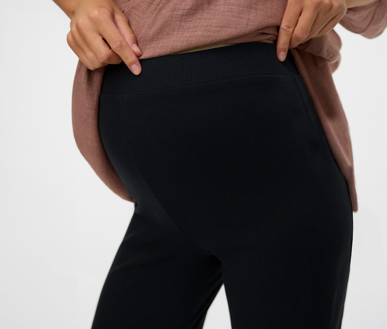 Žena ukazuje pás čiernych voľných legínsov MAMALICIOUS »MLEMILY«.