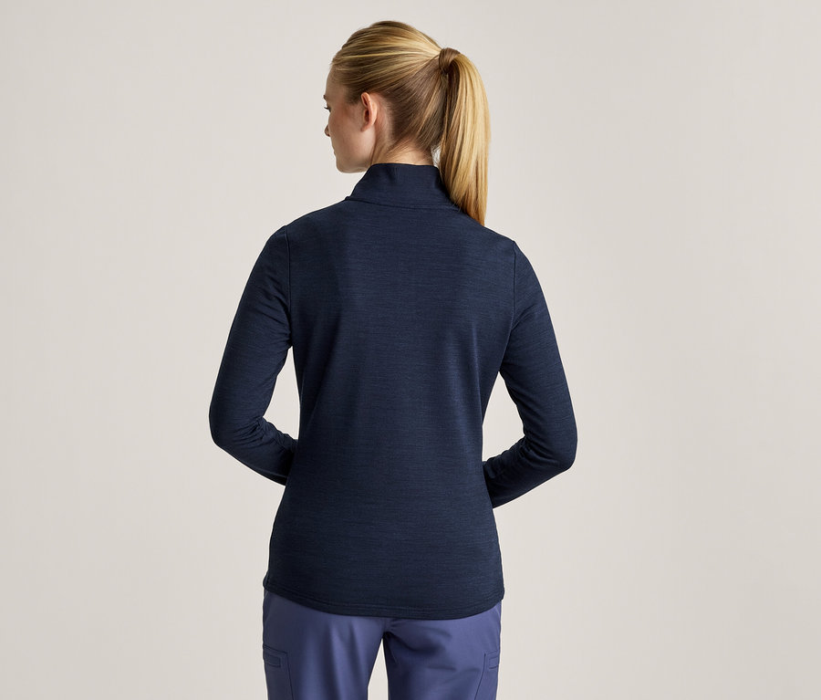 Žena zozadu s blond copom, oblečená v tmavomodrom tričku s dlhým rukávom a modrých nohaviciach.