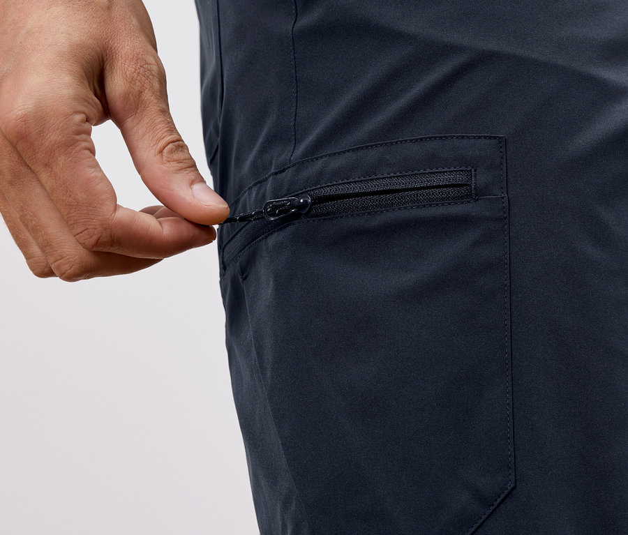 Detail záberu ruky zatvárajúcej zips na tmavomodrých nohaviciach.