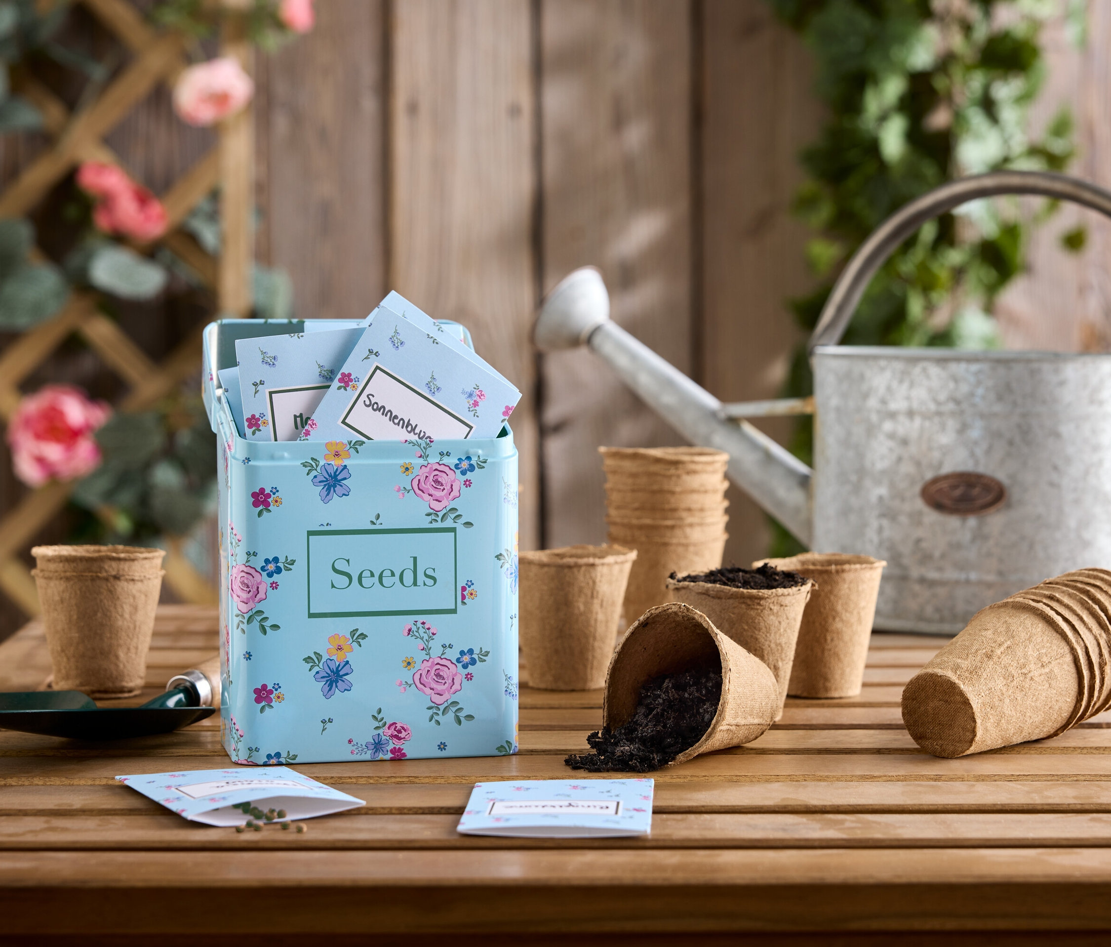 Sada kvetinových semien na drevenom stole s pozinkovanou kanvou a sadbovačmi.