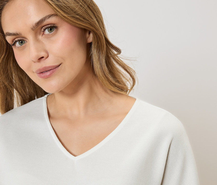 Portrét ženy s blond vlasmi v bielom svetri s výstrihom do V.