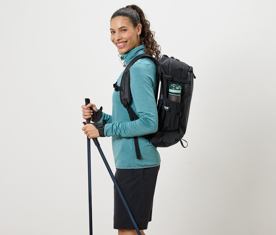 Žena v tyrkysovom roláku, s čiernym batohom a trekingovými palicami.