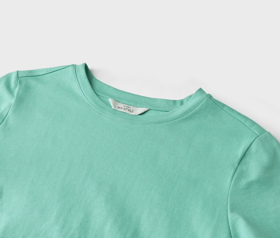 Detail záberu svetlotyrkysového trička s etiketou s nápisom "TCHIBO MY STYLE".