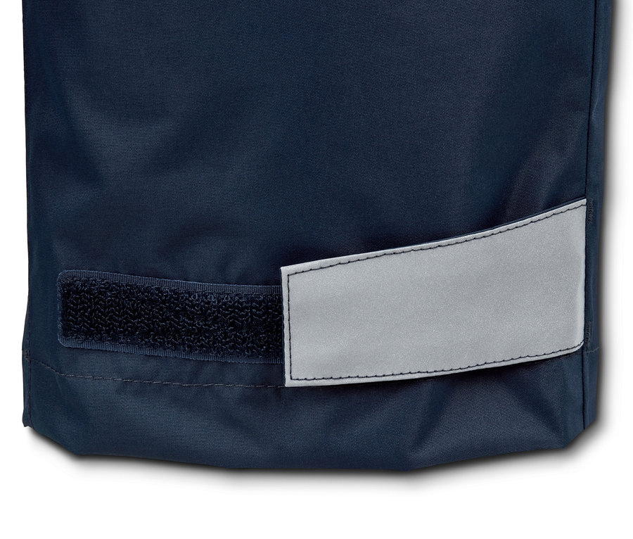 Detailný záber na spodnú časť nohavice nohavíc do dažďa z recyklovaného materiálu s reflexným prvkom a suchým zipsom.