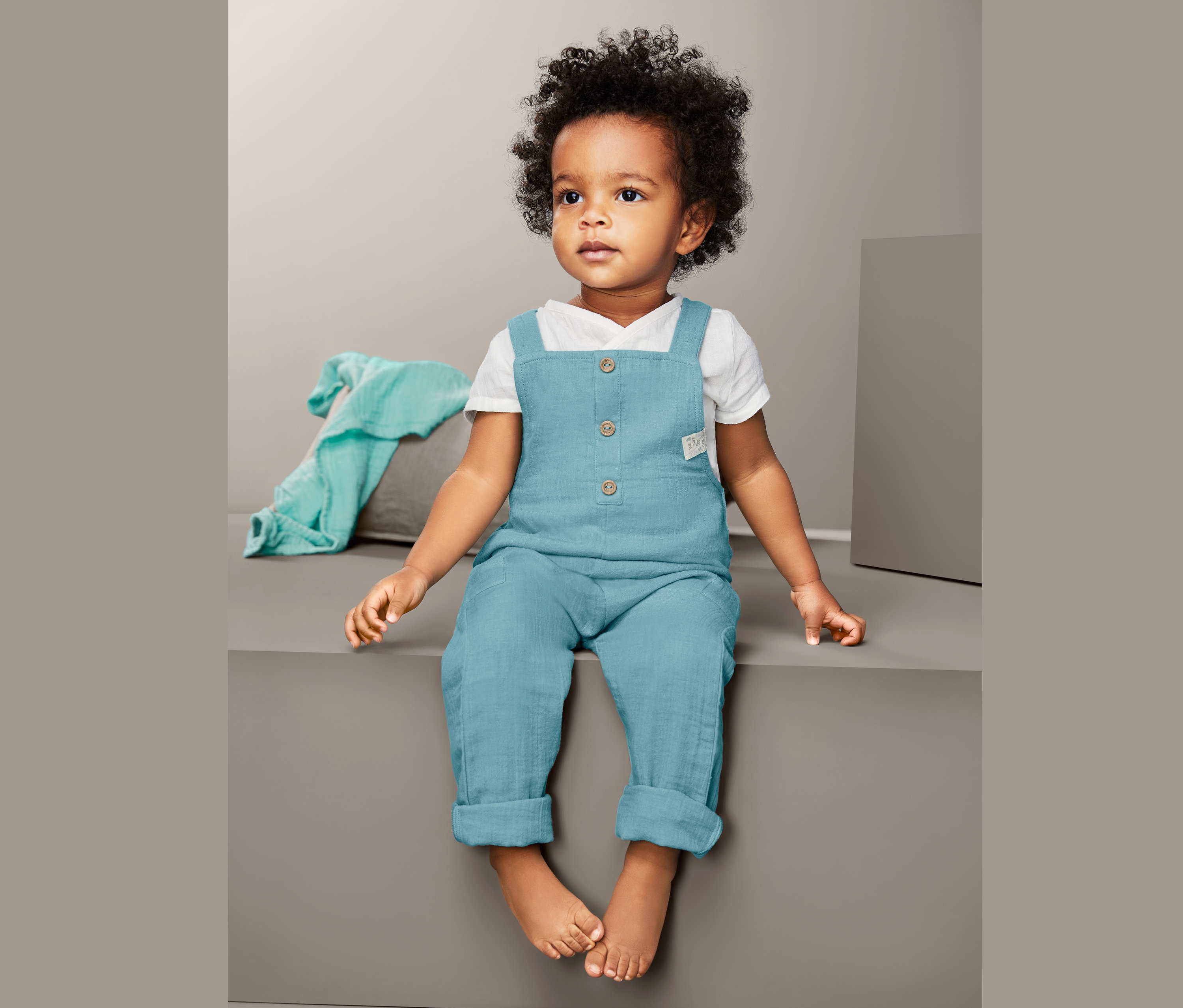 Dieťa sedí a má na sebe modré nohavice s náprsenkou.