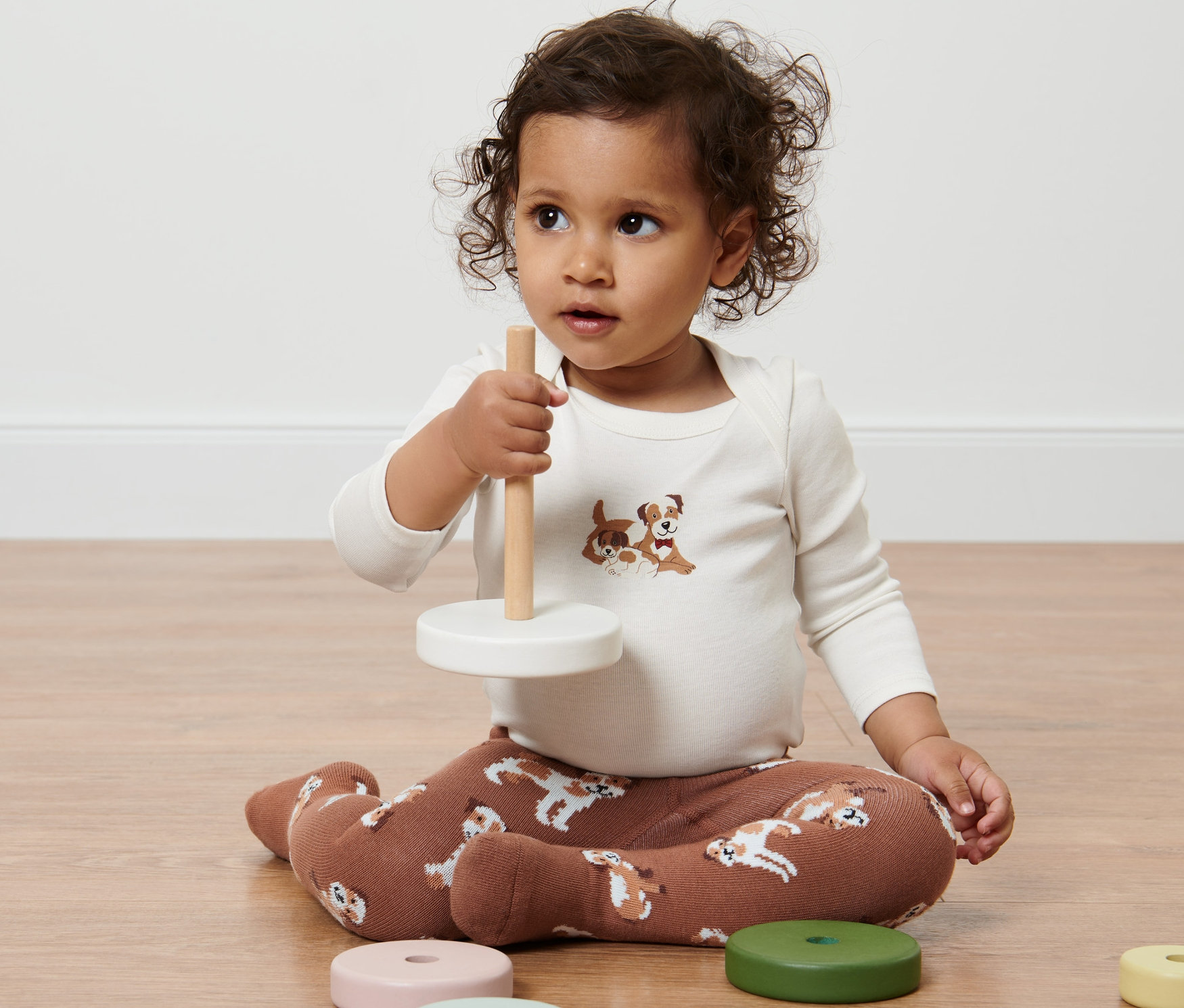 Dieťa sedí na podlahe a hrá sa s hračkou. Má na sebe detské pančuchy, 2 páry s potlačou psov.