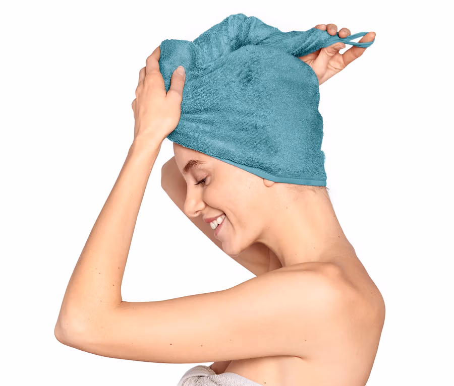 Žena si upravuje akvamarínový uterákový turban na hlave, telo má omotané uterákom.