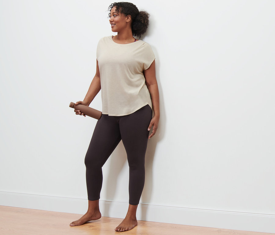 Žena drží hnedú fľašu na vodu, má na sebe béžové športové tričko a športové legínsy.