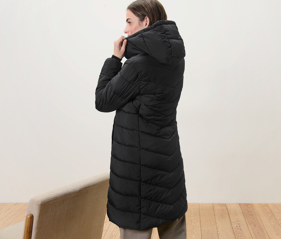 Žena si upravuje kapucňu na čiernom prešívanom kabáte s kapucňou.