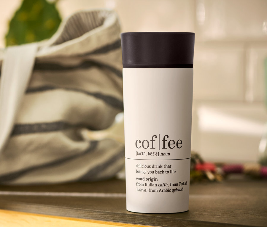 Biely hrnček na kávu To Go Coffee Dictionary s čiernym viečkom na stole.