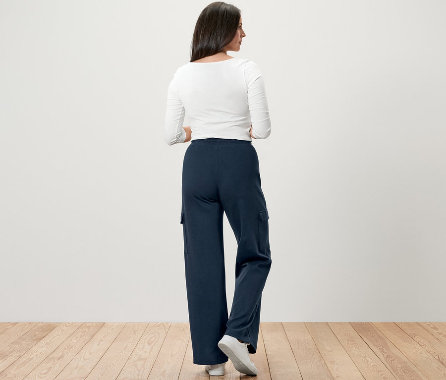 Žena stojí chrbtom k fotoaparátu a má na sebe tmavomodré teplákové nohavice s cargo vreckami.