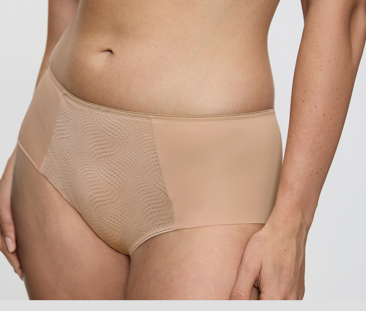 Detail trupu osoby v telových nohavičkách Triumph Essential »Minimizer Hipster X« s hladkou látkou po stranách a textúrovaným, vzorovaným sieťovaným panelom vpredu.
