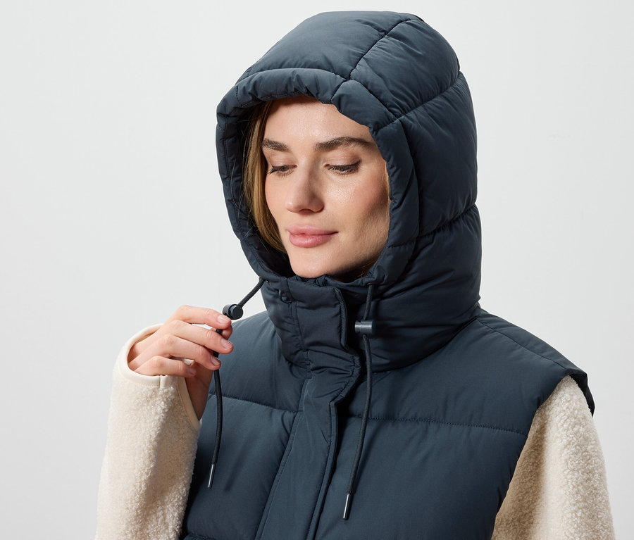 Žena si upravuje kapucňu tmavomodrej prešívanej vesty.