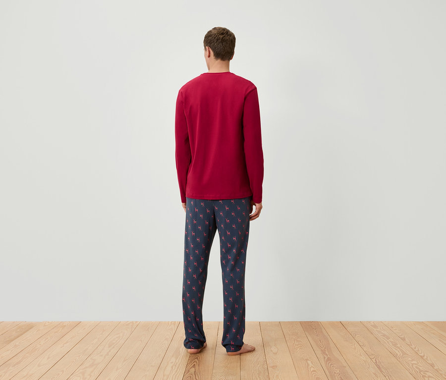 Muž chrbtom k fotoaparátu má na sebe červené pyžamové tričko s dlhým rukávom a tmavomodré pyžamové nohavice so vzorom sobov.