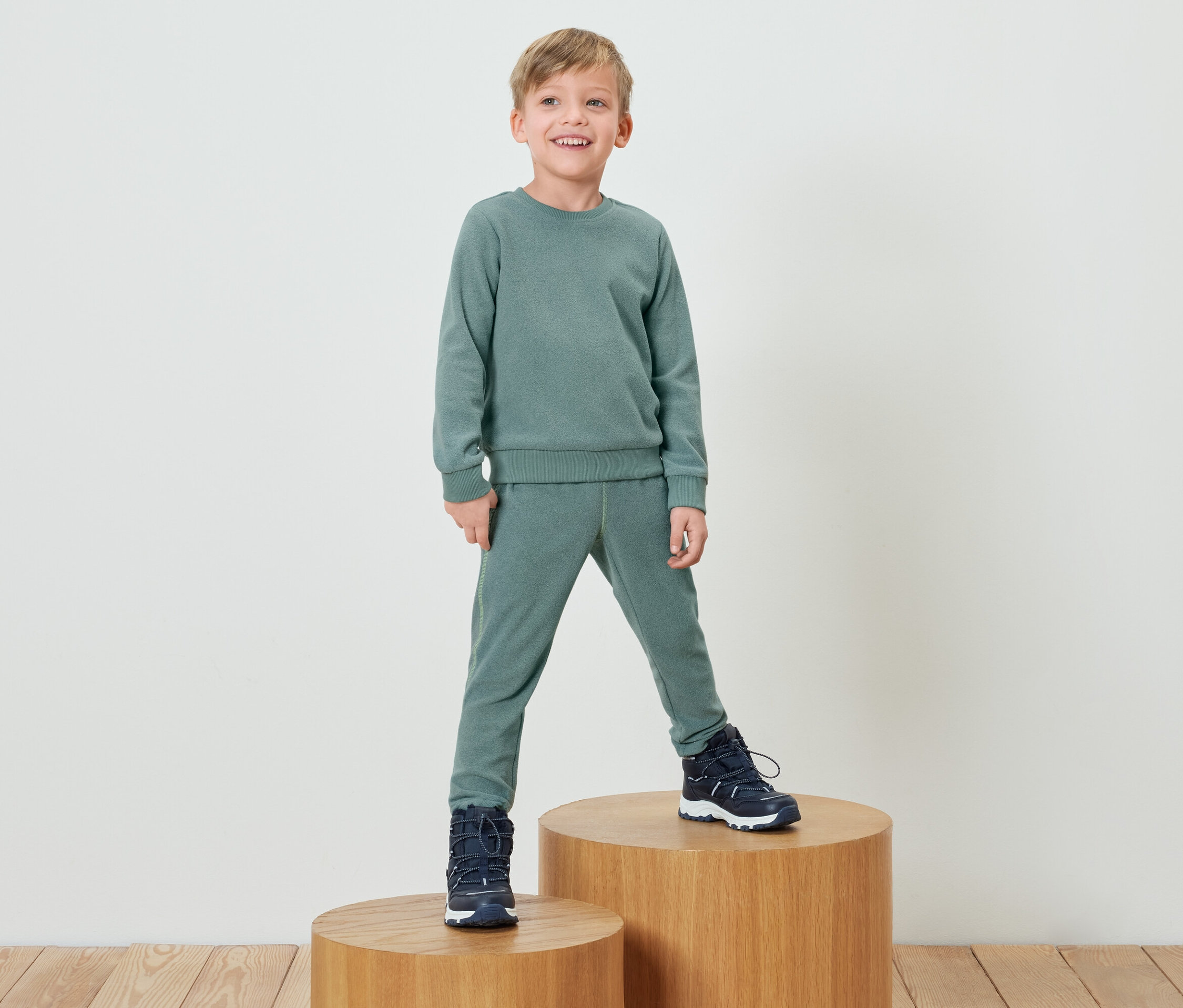 Chlapec v zelenej súprave stojí na drevenom podstavci.