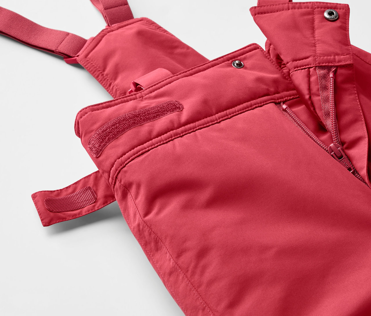 Detail červených lyžiarskych nohavíc s podbradníkom so zipsom.