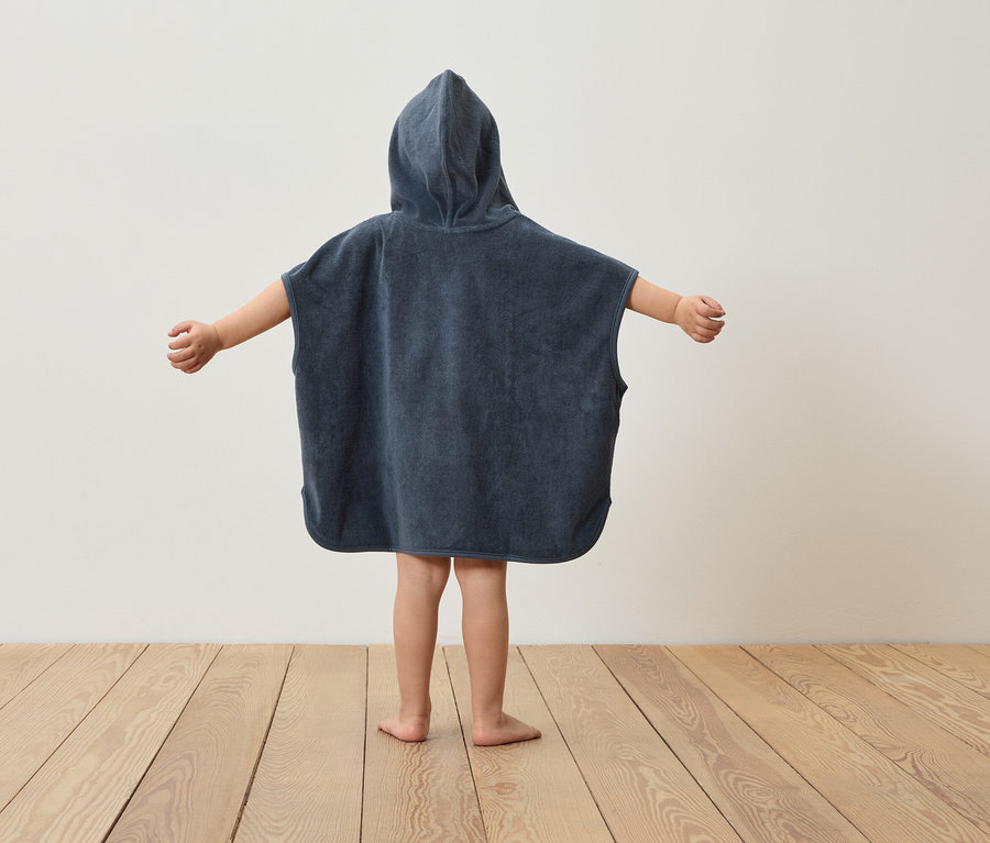 Dieťa stojí chrbtom a má na sebe tmavomodré pončo s kapucňou a roztiahnuté ruky.