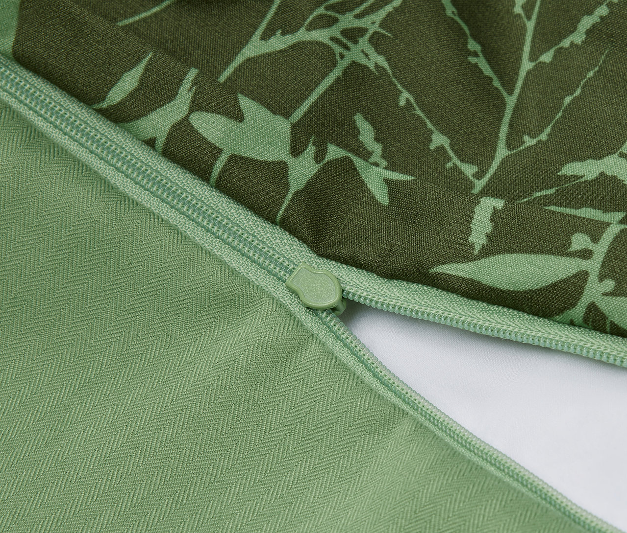 Detail zeleného obliečky na vankúš s kvetinovým vzorom a zipsom.