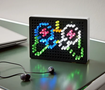 Na stole leží čierny svetelný box s farebnými svetlami zobrazujúcimi dvoch duchov, vedľa neho sú slúchadlá a notebook.