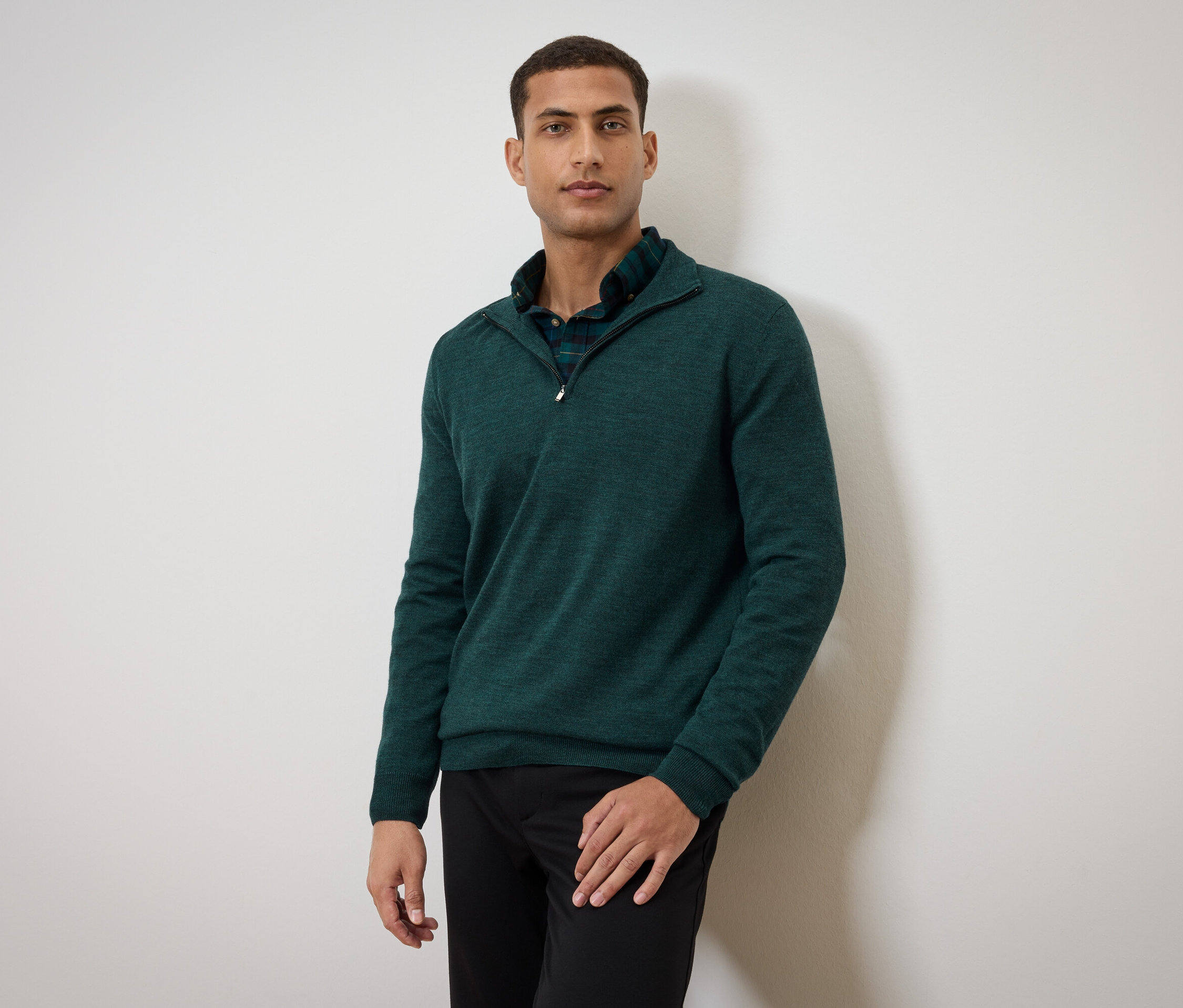 Muž pózuje v zelenom svetri a čiernych nohaviciach.