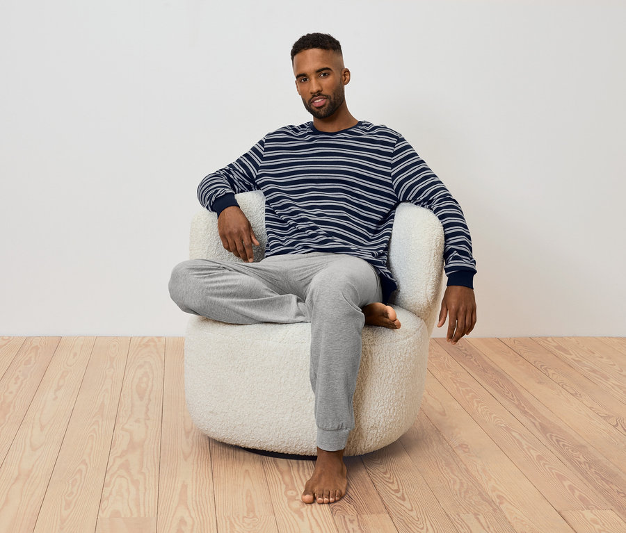 Muž sedí v kresle. Má na sebe pruhované tričko s dlhým rukávom a sivé tepláky.